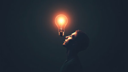 A vibrant light bulb glowing brightly above a person's head in a dark room, symbolizing the moment of inspiration and the birth of a new ideaの素材