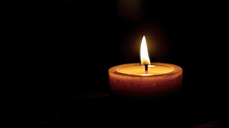 A single candle burning in a dark room, with its flame creating a dramatic and peaceful contrast against the surrounding shadows.の素材