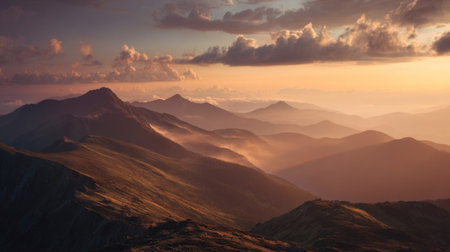 A breathtaking mountain landscape captured at sunset, showcasing layered peaks beneath soft clouds with warm hues illuminating the serene wilderness below.の素材