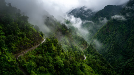 Explore a stunning mountain landscape enveloped in lush green vegetation and misty clouds, showcasing a winding road that invites travel and adventure in nature.の素材