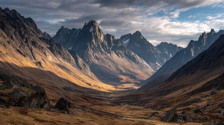 Explore a stunning mountain valley nestled between lofty peaks, illuminated by soft sunlight under a dramatic sky, showcasing the beauty of untouched wilderness.の素材