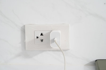 White wall power outlet with universal socket and white charger plugged in, minimalistic background,...