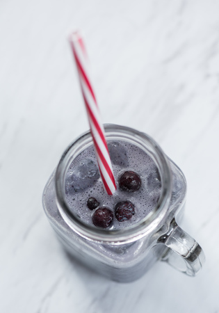 Closeup of a blueberry smoothie in a glass mug with a red and white striped straw on a marble countertopの写真素材