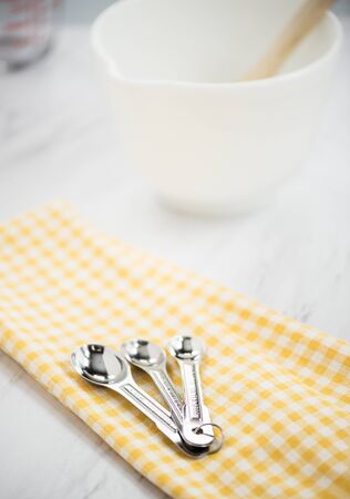 White mixing bowl and measuring spoons on a yellow plaid dishclothの写真素材