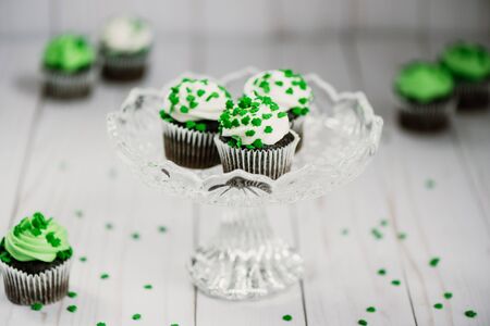 St. Patrick's Day chocolate cupcakes with green shamrock candies on a crystal serving dish and a wood countertopの写真素材