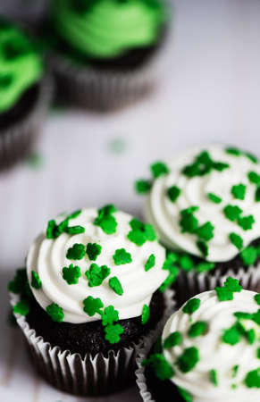 Closeup of chocolate cupcakes with white frosting and green shamrocks sprinkled on topの写真素材