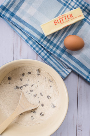 A bowl of chocolate chip cookie mix, stick of butter and an egg on a blue dishtowel