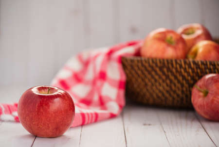 A shiny red apple sits on a wood top. Additional apples and a red plaid dish towel in a basket in background.の写真素材