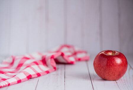 A single apple on a whitewashed wood top with a vintage red check dish towel.の写真素材
