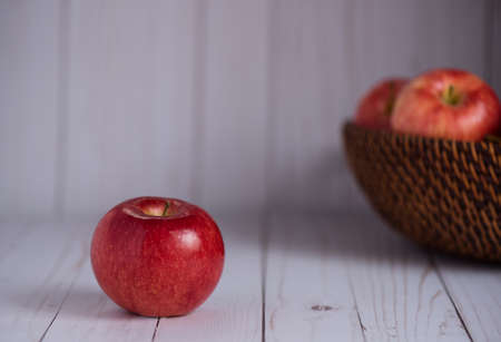 A shiny red apple sits on a wood top. Apples in basket in background.の写真素材