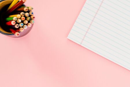A cup with colored pencils and a white notepad on a flat pink surfaceの写真素材
