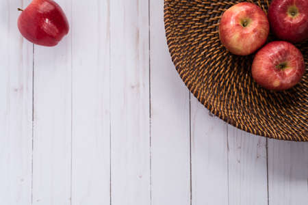 three apples in a woven basket and one single apple on top of a whitewashed wood countertopの写真素材