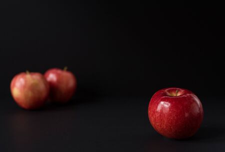 A shiny red apple isolated on black background. Two other apples out of focus in backgroundの写真素材