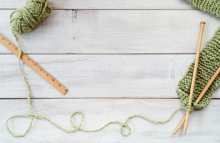 Knitting project with wooden needles, scarf, green yarn and wooden ruler on a whitewashed wood tableの写真素材