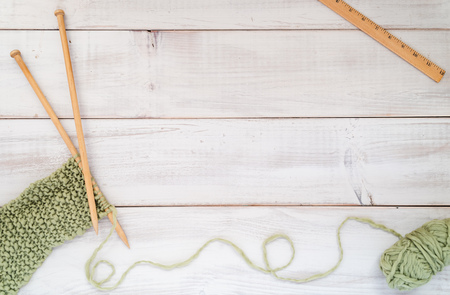 Knitting project with wooden needles, scarf, green yarn and wooden ruler on a whitewashed wood tableの写真素材