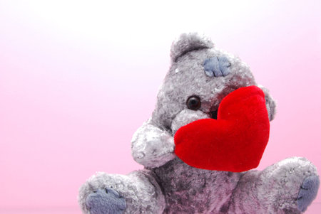 A shy teddy bear hiding behind a bright red heartの写真素材