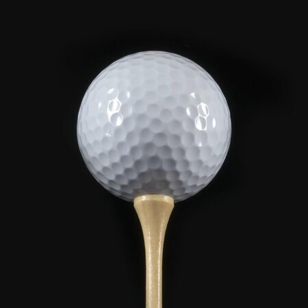 Golf ball on a tee against a black backgroundの写真素材