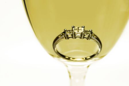 Trilogy diamond white gold engagement ring in a glass of white wine.の写真素材