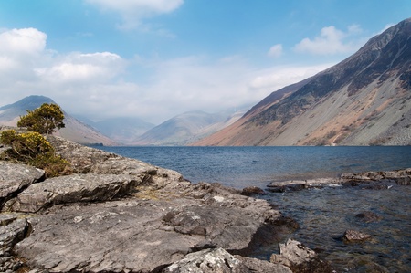 Rocks reaching out into a lake with mountains in the distanceの写真素材