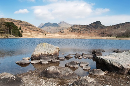 Rocks reaching out into a lake with mountains in the distanceの写真素材