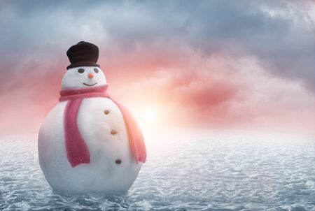 Happy snowman stands in the snow with a beautiful winter sunsetの写真素材
