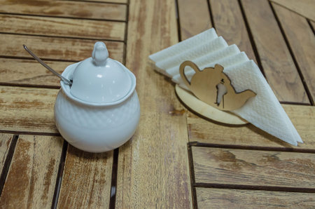 White porcelain sugar bowl and wooden napkin stand on the table in a cafeの写真素材