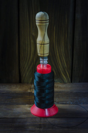Shoe awl next to the kapron thread, used by shoemakers and other tanners on a wooden background.