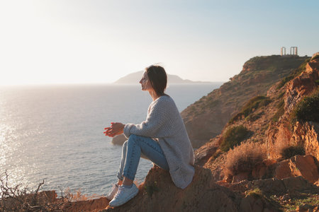 Traveler young woman sits on a cliff of cape Sounion and enjoys the moment.