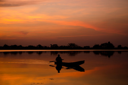 Silhouette of fisherman on boat in the sunrise,Thailandの写真素材