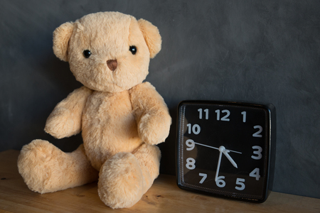 Teddy bear with clock,teddy bear sitting on wooden floor against cement wall backgroundの写真素材