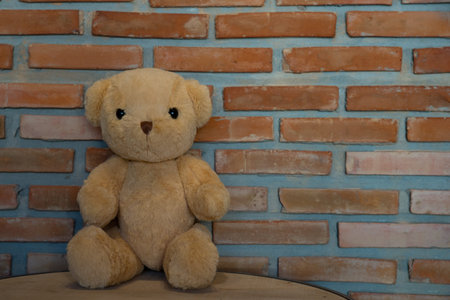 Cute teddy bear sitting on wooden floor against brick wall backgroundの写真素材