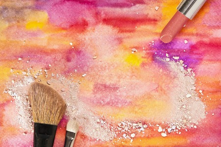Makeup brushes and lipstick on a vibrant yellow and purple background, with traces of powder and blush. Horizontal template for makeup artist's business card or flyer design, with plenty of copyspaceの写真素材