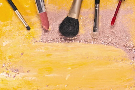 Makeup brushes and lipstick on a vibrant golden yellow background, with traces of powder and blush on it. A horizontal template for a makeup artist's business card or flyer design, with copyspaceの写真素材