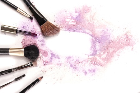 Makeup brushes, lip gloss and pencil on white background, with traces of powder and blush forming a frame.の写真素材