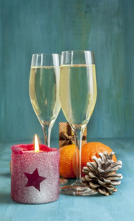 Photo for Christmas or New Year card. Two glasses of sparkling wine, burning candle with star shape on it, pine cone with snow, tangerines, and little present box in the background. Selective focusの写真素材