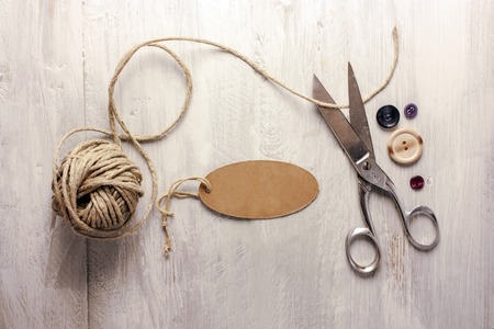 A photo of vintage scissors with a roll of twine, a tag with copyspace, and buttons, shot from above on light wooden boards background textureの写真素材