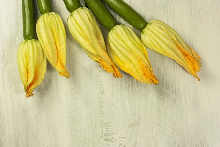 A photo of zucchini flowers, shot from above on a light wooden background, with copyspace. A vegan greeting cardの写真素材