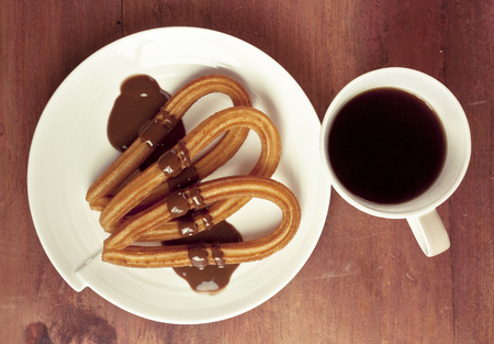 A closeup photo of churros with chocolate, traditional Spanish, especially Madrid, dessert, particularly for Sunday breakfast. On wooden background, shot from above. With a cup of black coffeeの写真素材