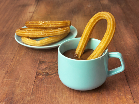 Churros, traditional Spanish, especially Madrid, dessert, often for Sunday breakfast, in the form of horseshoe, with a cup of chocolate on a wooden board texture, retro style, with copyspaceの写真素材