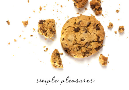 A photo of a crunchy chocolate chips cookie with crumbs around it, shot from above on a white...