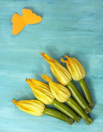 A photo of zucchini flowers with a paper butterfly, shot from above on a teal blue background, with copyspace. A vegan greeting cardの写真素材