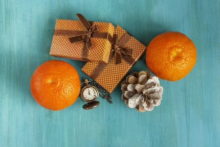 A photo of two gift boxes, tangerines, a pine cone, and a vintage chain clock showing midnight. A New Year or Christmas greeting card on a blue background with copyspace.の写真素材