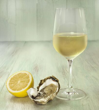 A photo of freshly opened oysters with a slice of lemon and a glass of white wine, on a blurred wooden background texture with copyspaceの写真素材