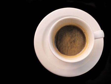 A photo of a white cup of coffee, shot from above on a black background with copyspaceの写真素材