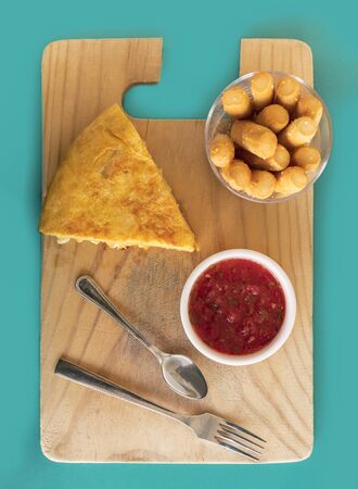 A photo of a tortilla, traditional Spanish snack, on a wooden board, with tomato sauce and bread sticks, shot from aboveの写真素材