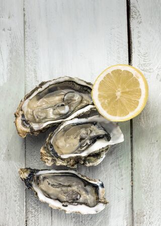 A photo of freshly opened oysters with a slice of lemon, on a wooden background texture with copyspaceの写真素材