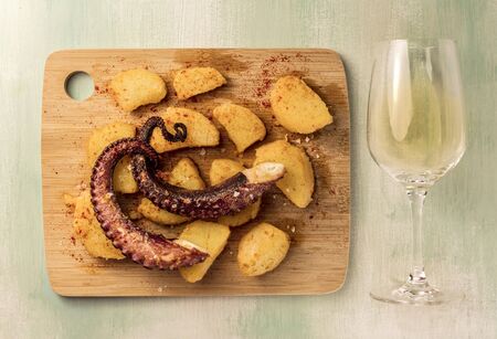A photo of an octopus with fried potatoes, typical Spanish dish, shot from above on a wooden board, with a glass of white wineの写真素材