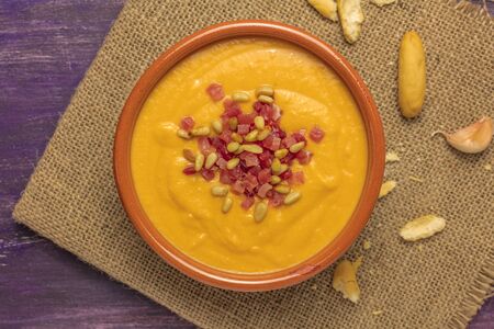 A photo of salmorejo, traditional Spanish cold soup, with bread sticks and crumbs, shot from above on a deep purple wooden textureの写真素材