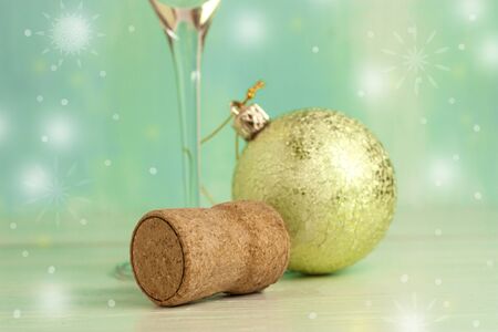 A photo of a sparkling wine cork with a blurred Christmas tree ball and a glass stem in the background. Selective focus and copyspaceの写真素材