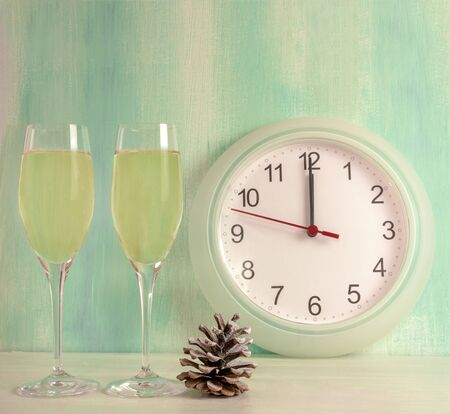 A photo of two flute glasses of sparkling wine with a pine cone, a clock about to strike midnight, and copyspaceの写真素材